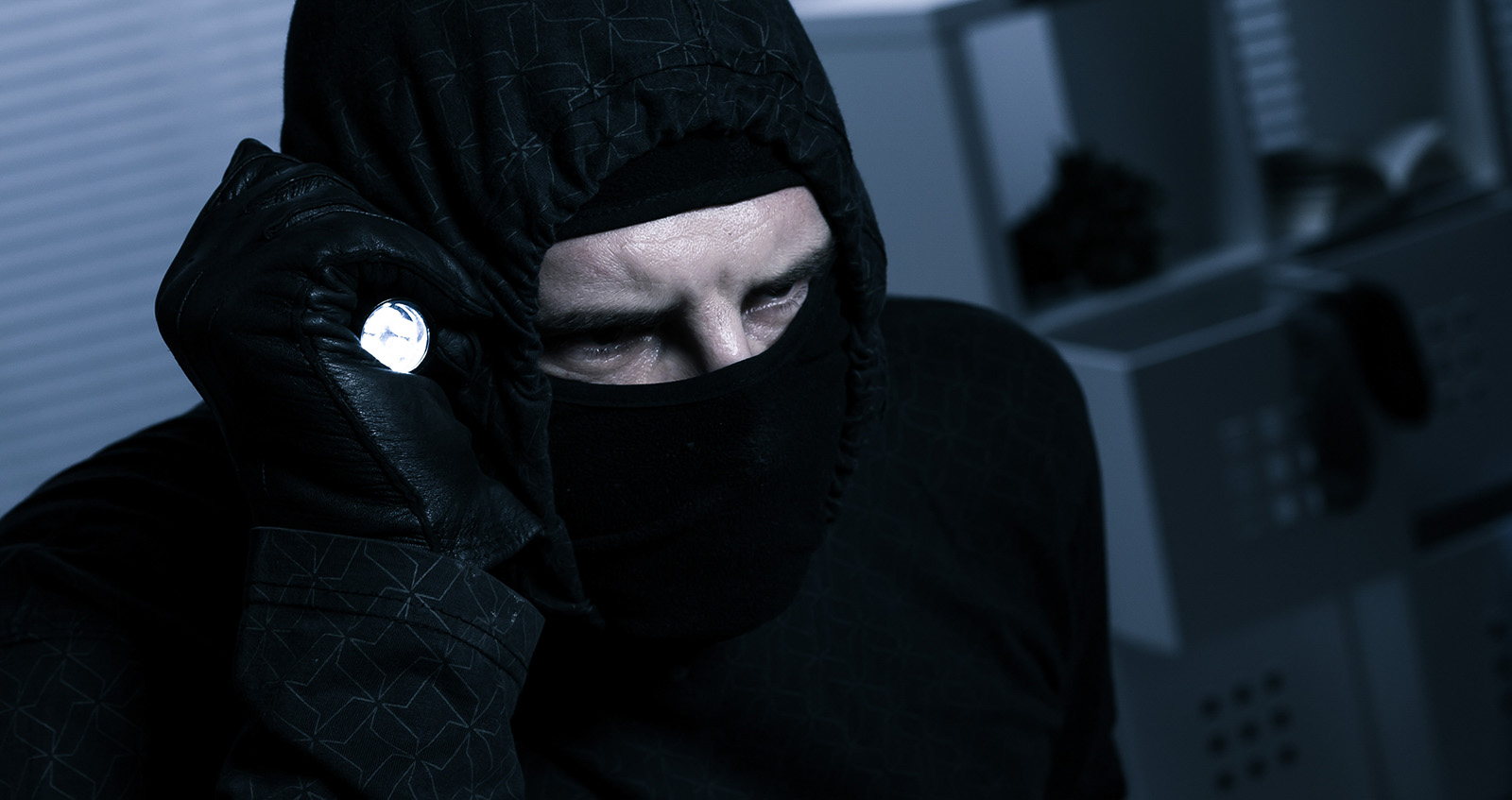 Masked burglar with flashlight during a burglary at night