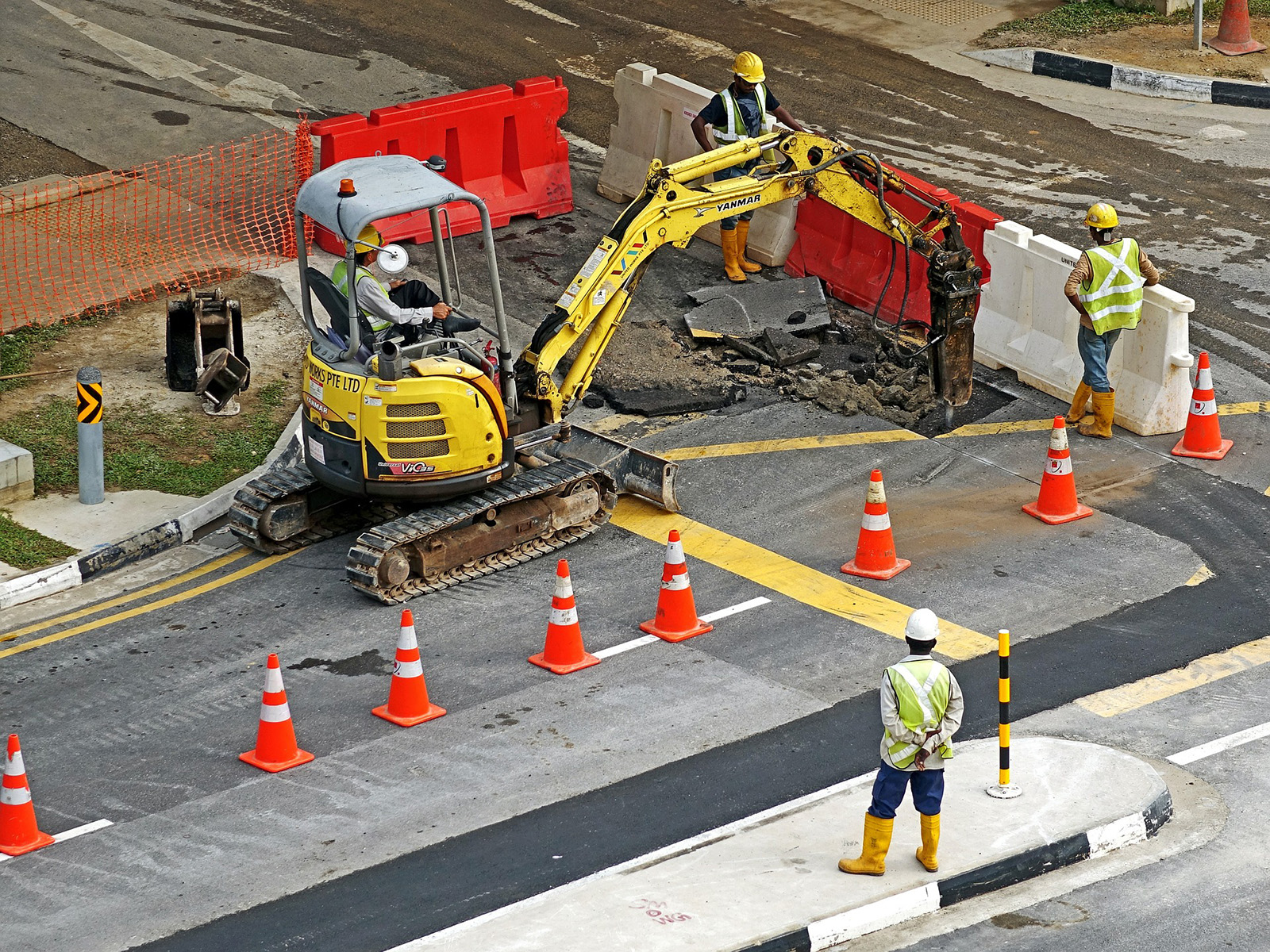 Construction site workers observing another working use a machine to dip up a road